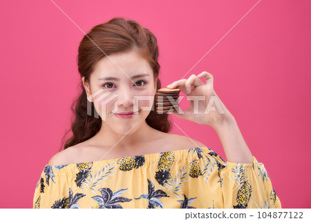 female model wearing a flower-patterned dress with a pink background and enjoying snacks 104877122