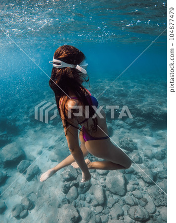 Young woman in bikini glides underwater in blue sea. 104877479