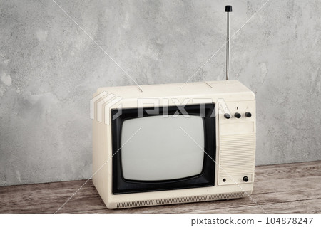 Vintage analog small TV set stand on wooden floor front grey concrete wall. 104878247