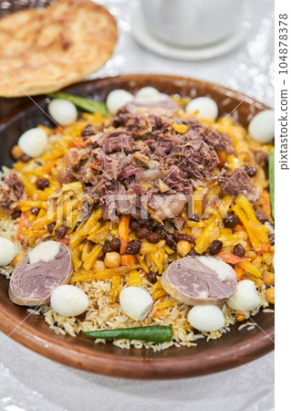 Rice with meat, carrots, onions, quail eggs and kazy in a plate of astau on the table. A traditional Uzbek dish called pilaf. A portion for three people. Rice with meat, carrots, onions, quail eggs and kazy in a plate of astau on the table. A traditional Uzbek dish called pilaf. A portion for three people. 104878378