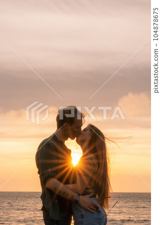 silhouettes in love romantic couple lovers hugging, kissing, touching, eye contact at sunset, sunrise on the background of the sea, the sun, the clouds in fiery red, orange colors 104878675