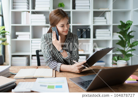 Consultant, advisor, Asian business woman working on the computer and using smartphone mobile talking work financial and marketing business planning company profits, marketing planning budget 104878727