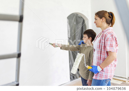 Mother and child son paint the wall with paint using roller and brush Mother and child son paint the wall with paint using roller and brush 104879636