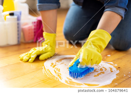 Woman in rubber gloves is using floor brush to cleaning floor 104879641