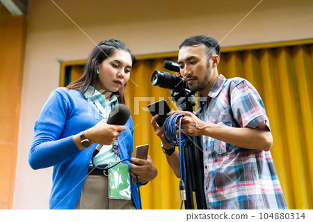 a reporter and the cameraman looking for information at the cameraman's phone 104880314