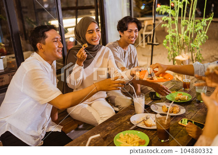 Young Asian woman in hijab serves food on a plate to friends Young Asian woman in hijab serves food on a plate to friends 104880332