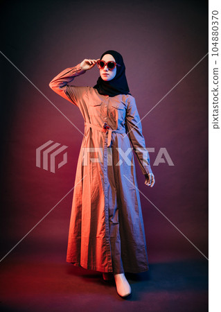 muslim woman wearing black hijab and long dress holding sunglasses looking sideways 104880370