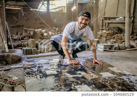 Smiling stonemason squats while washing large squares of stone Smiling stonemason squats while washing large squares of stone 104880529