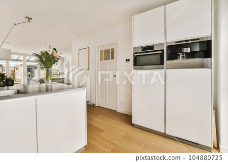 a kitchen with wood flooring and white cabinets in the center of the photo is an open door leading to another room 104880725