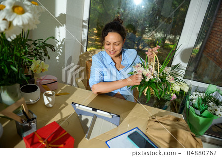 Woman florist holds a wicker basket with beautiful flowers, discussing orders for floral arrangements for festive event 104880762