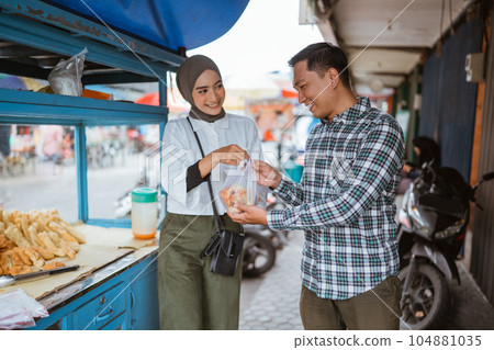 a beautiful girl wearing a hijab while using tongs sells various kinds of fried food with a cart 104881035