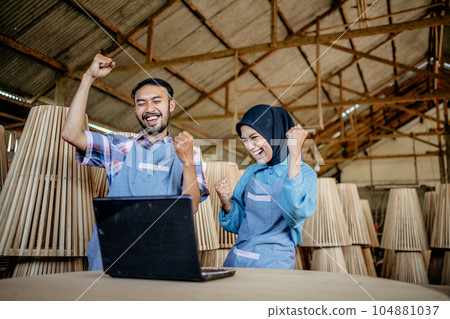 Asian businessman and woman in hijab with victory gesture looking at laptop 104881037