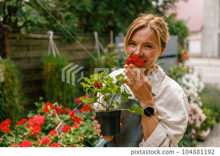 Woman florist business owner is inhaling aroma of houseplant on background of floral store Woman florist business owner is inhaling aroma of houseplant on background of floral store 104881192