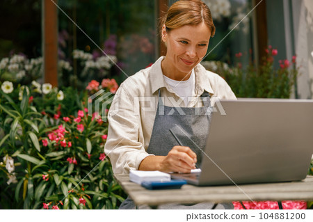 Professional flower shop owner florist using laptop and writing on notebook at flower shop Professional flower shop owner florist using laptop and writing on notebook at flower shop 104881200