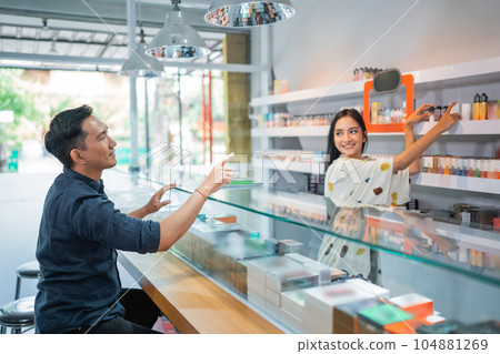 female shopkeeper helping the male customer to take the liquid female shopkeeper helping the male customer to take the liquid 104881269