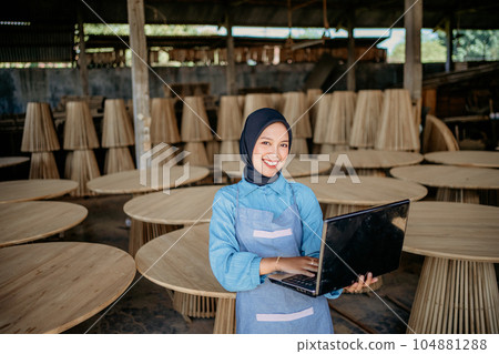 Smiling toothy veiled woman using laptop computer in craft shop Smiling toothy veiled woman using laptop computer in craft shop 104881288