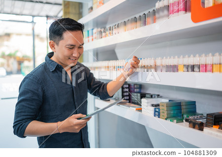 male shopkeeper looking at the digital tablet while checking the liquid stock 104881309