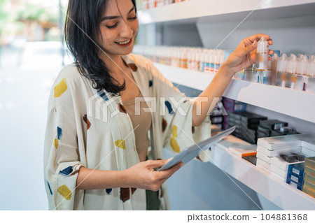 beautiful shopkeeper looking at the digital tablet while checking the liquid stock beautiful shopkeeper looking at the digital tablet while checking the liquid stock 104881368