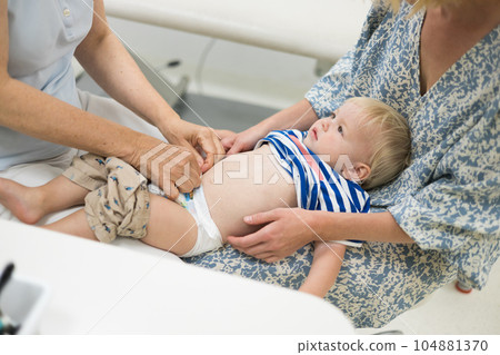 Infant baby boy child being examined by his pediatrician doctor during a standard medical checkup in presence and comfort of his mother. National public health and childs care care koncept Infant baby boy child being examined by his pediatrician doctor during a standard medical checkup in presence and comfort of his mother. National public health and childs care care koncept 104881370