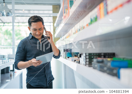 male shopkeeper looking at the digital tablet checking the liquid stock male shopkeeper looking at the digital tablet checking the liquid stock 104881394