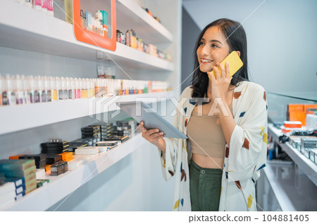 female shopkeeper checking the liquid stock while calling on phone female shopkeeper checking the liquid stock while calling on phone 104881405