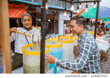 a pretty girl in a veil sells es campur using a scoop to get coconut milk 104881430