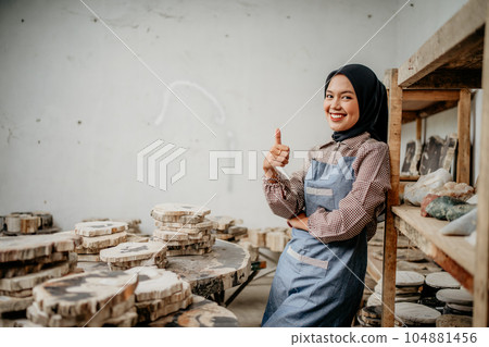Muslim woman smiling with thumbs up leaning on a shelf Muslim woman smiling with thumbs up leaning on a shelf 104881456