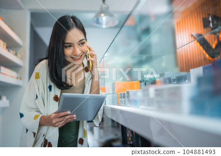 female shopkeeper calling on phone while checking the vape mods stock 104881493