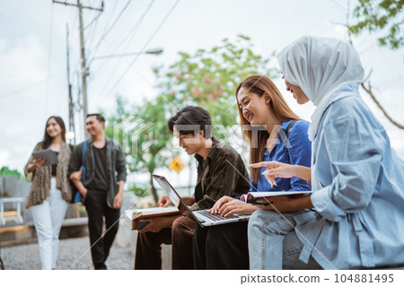 Group of young students studying using a laptop in an outdoor cafe Group of young students studying using a laptop in an outdoor cafe 104881495