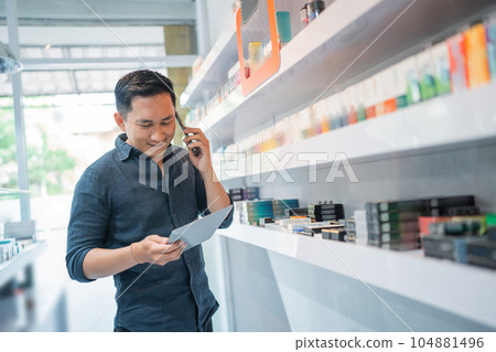 male shopkeeper standing beside the store shelf while calling on phone male shopkeeper standing beside the store shelf while calling on phone 104881496