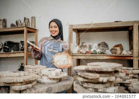 Muslim businesswoman with toothy smile holding a stone cut craft Muslim businesswoman with toothy smile holding a stone cut craft 104881577