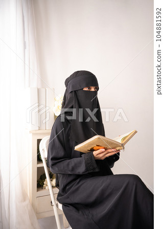 muslim woman wearing black hijab long dress is sitting reading al qur'an muslim woman wearing black hijab long dress is sitting reading al qur'an 104881592