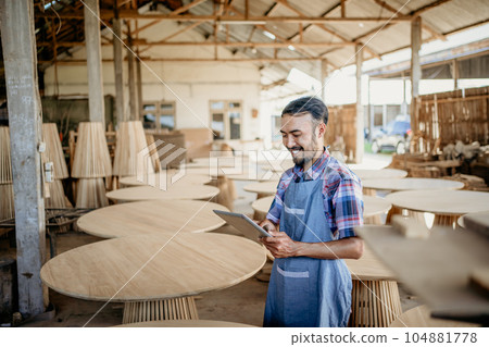 Asian businessman using a tablet computer standing craft shop in the background Asian businessman using a tablet computer standing craft shop in the background 104881778