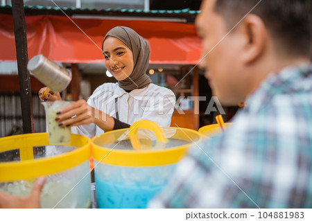 a pretty girl in a veil sells es campur using a scoop to get coconut milk 104881983