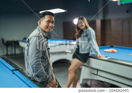 male billiard player standing leaning on the billiard table holding the stick 104882045