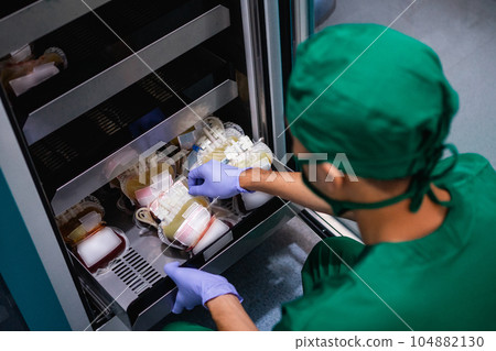 doctor in uniform with rubber gloves removes blood bag from storage 104882130