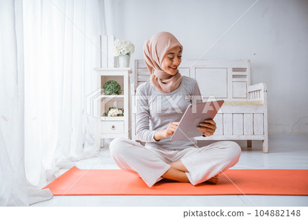 Muslim hijab woman watching exercise home workout tutorial from tablet in room Muslim hijab woman watching exercise home workout tutorial from tablet in room 104882148