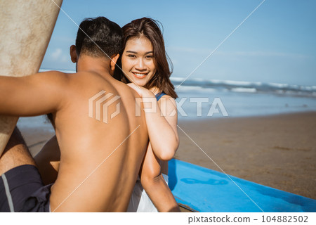 romantic beautiful woman hugging her partner sitting by the surfboard 104882502