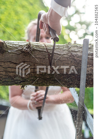 Young bridal couple groom bride sawing a tree trunk together german wedding tradition 104882565