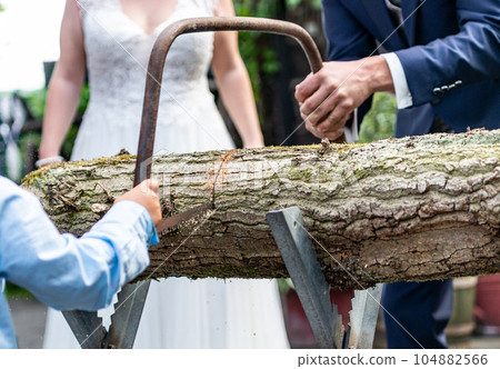 Young bridal couple groom bride sawing a tree trunk together german wedding tradition Young bridal couple groom bride sawing a tree trunk together german wedding tradition 104882566