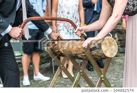 Young bridal couple groom bride sawing a tree trunk together german wedding tradition 104882574