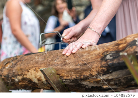 Young bridal couple groom bride sawing a tree trunk together german wedding tradition 104882579