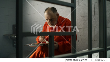 Elderly prisoner eats food sitting in prison cell in jail Elderly prisoner eats food sitting in prison cell in jail 104883220