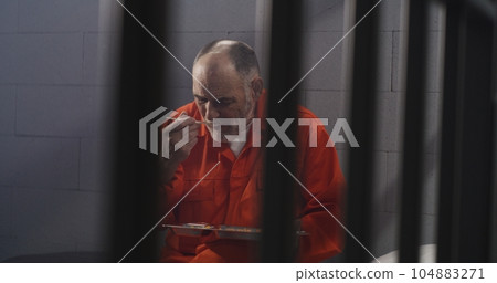 Prison guard gives food to prisoner through metal bars 104883271