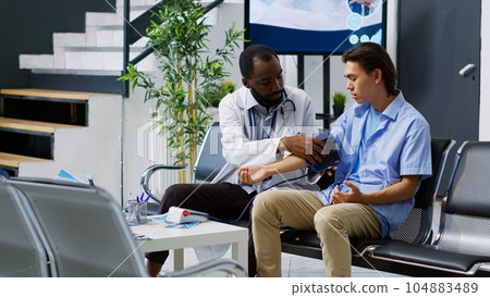 Traumatologist doing cardiology exam with asian patient, measuring blood and pulse pressure. Elderly doctor checking man hypertension using medical tonometer insturment in hospital lobby 104883489