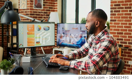 Remote employee checking online business analytics statistical data charts while working from home in stylish apartment. Teleworker optimizing market performance indicators with tv as background noise 104883491