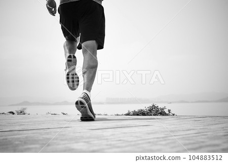 close-up shot of legs of an asian runner running by the sea, rear view, black and white 104883512