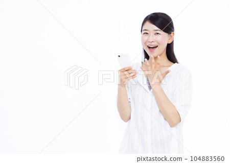 A woman in her thirties who is surprised with a smile holding a smartphone in front of a white background 104883560