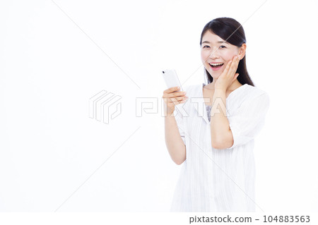 A woman in her thirties who is surprised with a smile holding a smartphone in front of a white background 104883563
