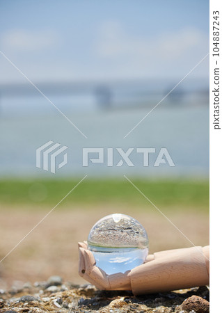 沙灘上人體模型娃娃一隻手和透明水晶玻璃球的風景 沙灘上人體模型娃娃一隻手和透明水晶玻璃球的風景 104887243